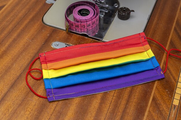 Mãos De Uma Mulher Desconhecida Costurando Máscaras Coloridas Em Uma Máquina De Costura, Enfatizando A Proteção Contra A Pandemia De Covid-19 Com Um Padrão De Arco-íris.