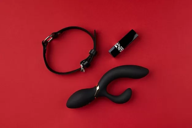 Um Vibrador Preto E Um Colar De Couro Preto Exibidos Contra Um Fundo Vermelho Vibrante, Enfatizando Acessórios De Bem-estar Sexual Masculino.