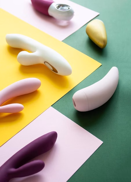 Uma Coleção De Diversos Produtos De Bem-estar Sexual, Incluindo Vibradores E Brinquedos, Exibidos Contra Um Fundo Colorido Em Rosa, Verde E Amarelo.