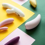 Uma Coleção De Diversos Brinquedos Sexuais Coloridos Exibidos Sobre Um Fundo Rosa, Verde E Amarelo.