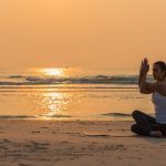 Uma Jovem Mulher Saudável Praticando Yoga Na Praia Ao Amanhecer, Fazendo Uma Pose De Meditação Com Ondas Suaves Ao Fundo.