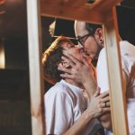 Um Casal Se Beijando Em Uma Loja De Produtos Para Adultos Aconchegante, Em Pé Ao Lado De Um Suporte De Exibição Cheio De Vários Produtos.