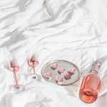 Vista De Cima De Taças De Champanhe Brilhantes E Uma Garrafa De Vinho Rosé Espumante Ao Lado De Uma Vela Rosa E Decorações Em Forma De Coração Em Uma Cama Branca, Criando Uma Atmosfera Romântica E íNtima.